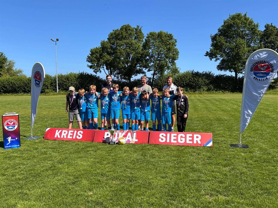 Jugendmannschaft in blauem Trikot mit Medaillen und Pokal am Banner „Kreispokalsieger“